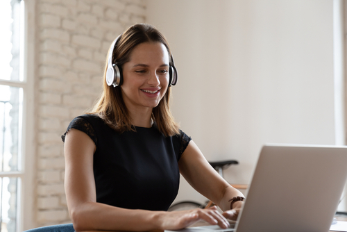 Smiling,Woman,Wearing,Wireless,Headphones,Working,Typing,On,Notebook,Sit